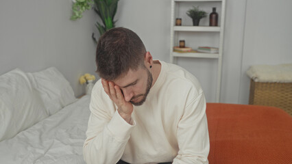 Fototapeta premium Man sitting on bed with hand on face and head in hand gesture inside building; quiet reflection sadness.