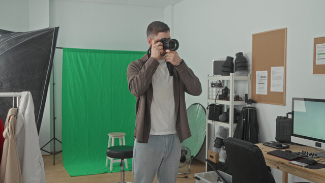 Man holding a dslr camera, checking settings and occasionally raising it to his eye in studio; focused creativity.
