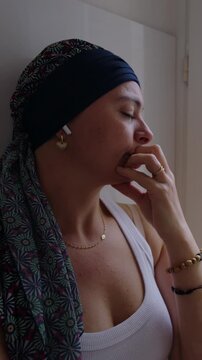 Woman undergoing chemotherapy resting by window at home, headscarf cancer patient with eyes closed in fatigue, recovery journey, vulnerability, quiet pain and emotional resilience