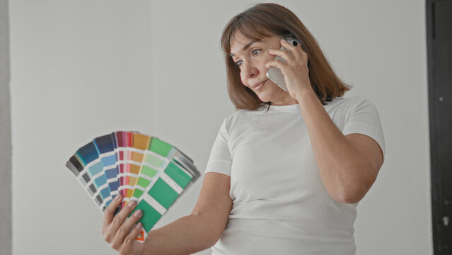 Woman holding smartphone to ear and paint swatches while choosing colors inside a building; quiet contemplation.