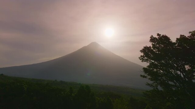 Majestic Volcano Arenal rises above lush Costa Rica rainforest during golden sunrise. Soft morning light illuminates the conical peak while mist drifts across dense jungle canopy below.