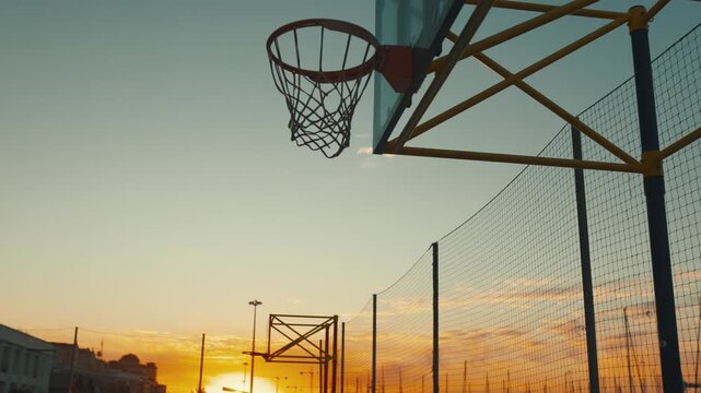 Outdoor basketball court with hoop silhouette at sunset
