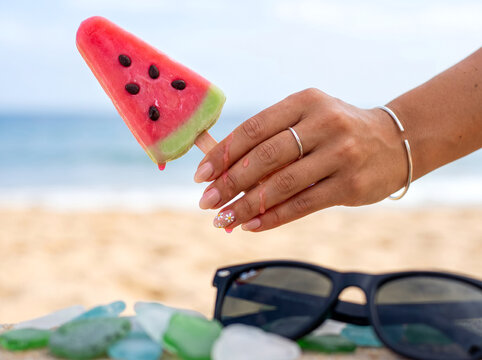 Hand holding a dripping watermelon popsicle on a sunny sandy beach