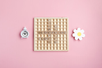 Obraz premium Wooden letters Menopause with alarm clock, pink background. Women hormone therapy concept. Estrogen replacement therapy awareness design.