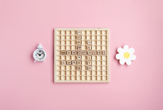 Wooden letters Menopause with alarm clock, pink background. Women hormone therapy concept. Estrogen replacement therapy awareness design.
