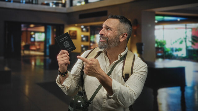 Man middle age hispanic grey hair backpacker holding passport with palm up gesture in hotel building lobby; travel frustration.