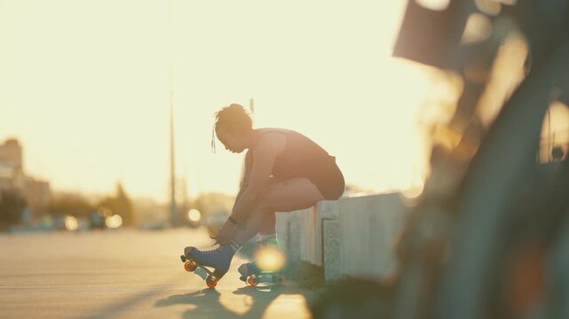 Tattooed woman tying laces on roller skates at sunset