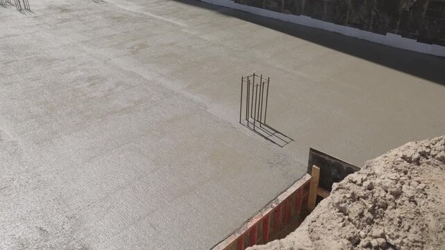 Fresh wet cement hardening and solidifying on a construction site, creating a durable concrete foundation for a new building as the shadow of a steel rebar moves across the surface