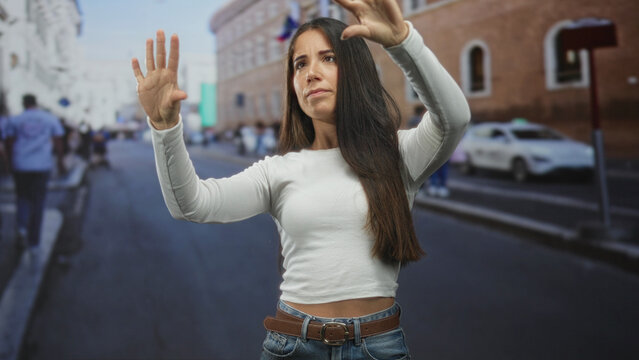 Woman reaching forward with hands raised and palms out as if touching an invisible screen on a city street; focus concentration.