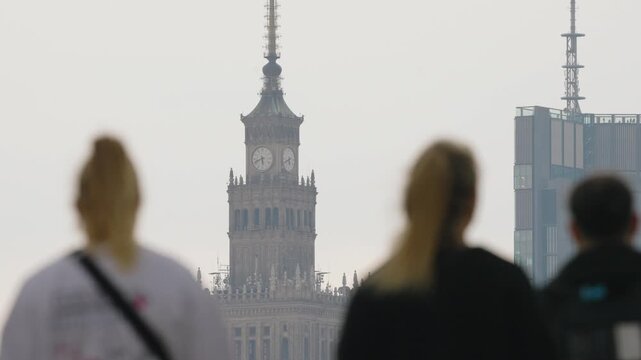 Cinematic Warsaw skyline with Palace of Culture and Science and modern skyscraper in focus under overcast soft light, blurred foreground pedestrians walking across urban square, spring city atmosphere