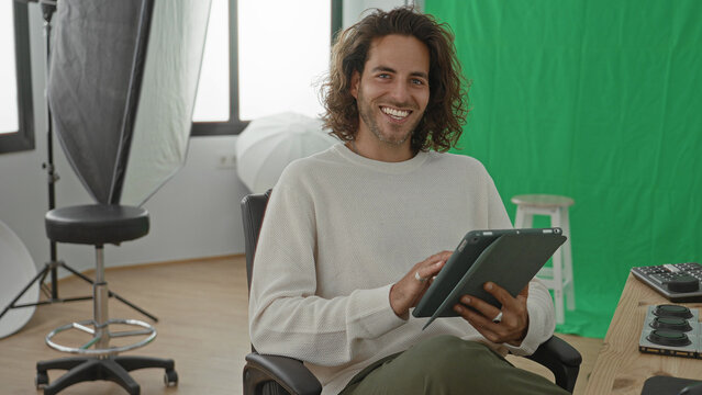 Man photographer taps tablet with hands in studio green screen and softbox visible; focused creativity.