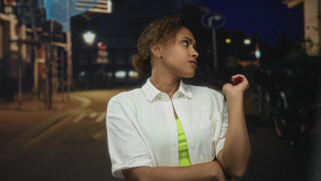 Woman holding feather duster with crossed arms on city street at night, looking sideways with a dismissive glance; indifference.