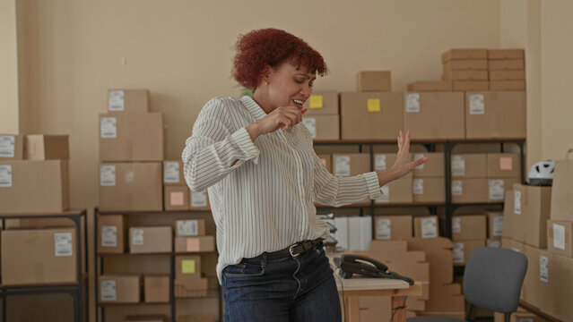 Woman singing with candy in hand in a building packed with cardboard boxes and parcels; workplace joy.