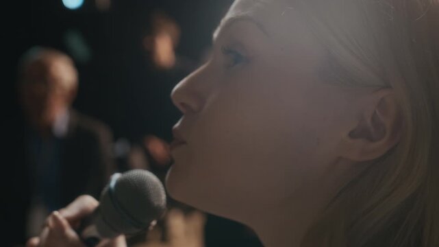 Closeup handheld shot young blonde Caucasian female speaker holding microphone giving presentation standing in front of audience at business conference