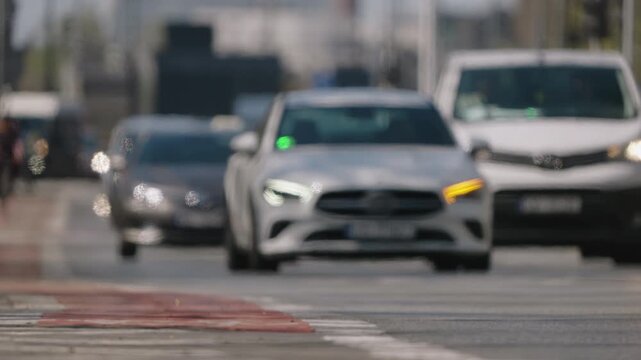 Defocused low angle view of dense city traffic approaching camera, abstract motion of vehicles with heat haze and shimmering air above asphalt, bright sunny day urban scene