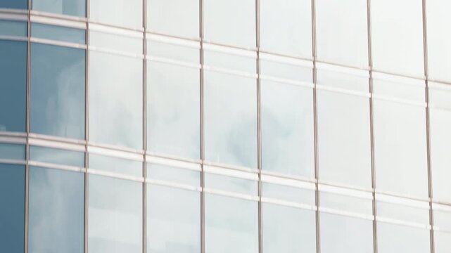Low to high angle camera movement along skyscraper windows, smooth upward motion ending in open sky, daytime city architecture shot with modern glass facade