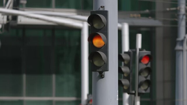 Cinematic close up of city traffic signal changing color, red to green transition, business buildings blurred in background under natural daylight
