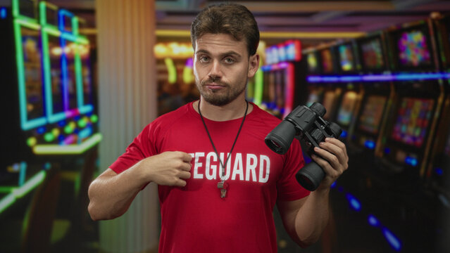 Man holding binoculars and pointing finger at slot machine in casino building; boredom surveillance duty.