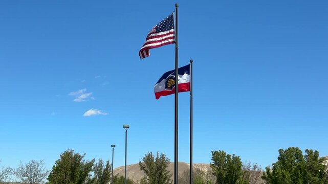 The American Flag and the Utah State Flag flying in the wind against blue sky and mountains 