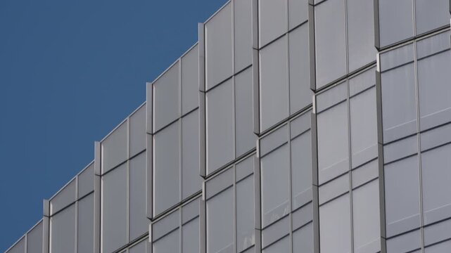 Vertical pan up view of tall glass high rise building, camera moving from street level to roofline and sky, clean daylight and modern urban architecture detail
