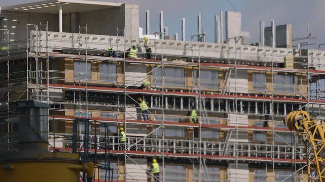 Cinematic construction site facade, workers on scaffolding working on exterior, foreground machinery creating strong heat haze under intense sunlight, modern architecture development scene