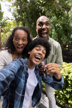 Family laughing and taking selfie in garden patio in casual clothes holding car keys and smartphone