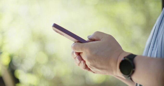 Senior Asian man holding purple phone, tapping, swiping, adjusting grip outside, wearing smartwatch