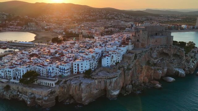 Aerial sunset shot of Peniscola resort town in Spain near Valencia, drone orbiting view of evening in Peniscola with Peniscola castle and lighthouse, vacation in Spain