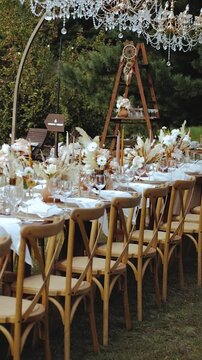 Vertical video. Wooden outdoor wedding table decorated with candles and dried flowers in pastel colors for a boho wedding dinner, plates and wine glasses. Wedding decor, banquet decor, tent decor.