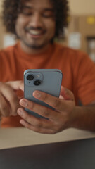 Fototapeta premium Smiling man holding smartphone, finger tapping screen amid cardboard boxes and laptop on desk in building; satisfaction entrepreneurship.