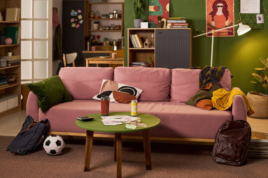 Wide shot of student living room showing backpacks, soccer ball, study books, bills, and drinks, illustrating busy college routine. Useful for education, youth lifestyle, budgeting themes
