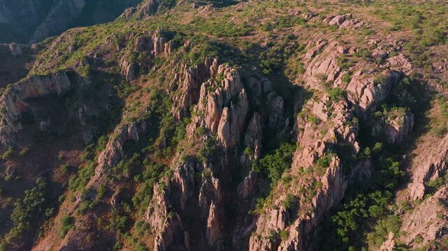 Stunning aerial footage of Sierra Madre Occidental mountain range in Durango, Mexico. Pink granite rock formations and lush green vegetation cover rugged terrain during golden hour light.