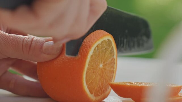 Closeup campsite hand peeling orange slice. Knife trims rind on white board, tactile motion and steady grip, bright citrus texture and droplets, precise prep for camping drink or snack.