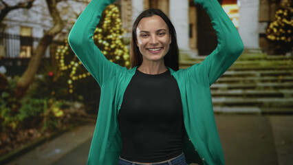 Fototapeta premium Woman smiling with arms raised and hands visible in front of building steps and twinkling lights near an entrance; joy celebration.