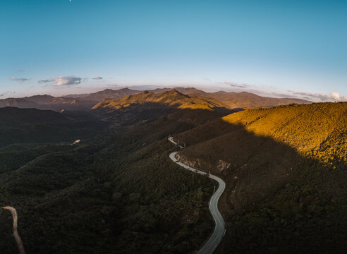 Fotografia a&eacute;rea das montanhas da Serra da Mantiqueira, no sul de Minas Gerais, com estrada serpenteando entre os picos e compondo um cen&aacute;rio deslumbrante para quem ama explorar e viajar.