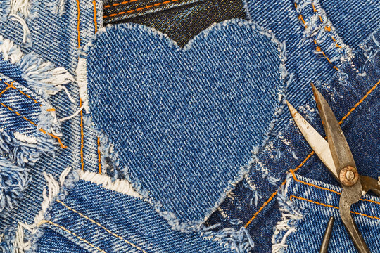Denim heart shape cut from fabric surrounded by other denim pieces and scissors placed nearby in a workspace