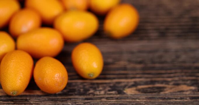 small orange fruits of juicy fresh and fragrant kumquat on a black table, oval oblong kumquat fruit scattered on a black table made of pine wood