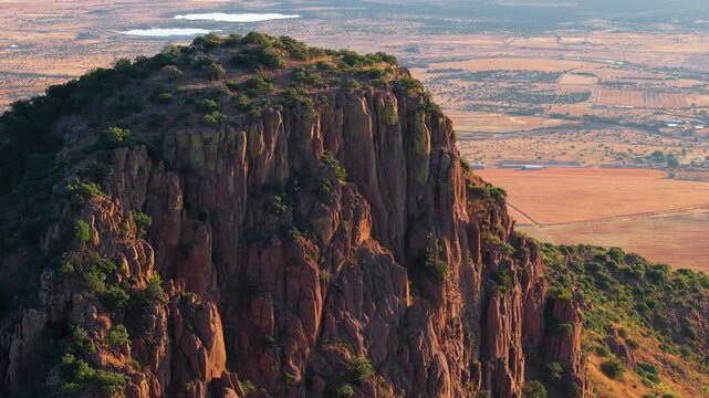Aerial drone footage showcases majestic red rock mesa with dramatic vertical cliff formations and lush green vegetation on top.