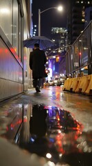 Fototapeta premium Individual walking with an umbrella along a city sidewalk at night, illuminated buildings and reflections visible in a puddle on the ground