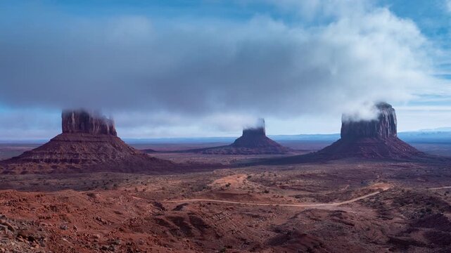 Time-lapse of iconic monuments in Arizona showing dramatic fog rolling over red sandstone buttes in Monument Valley. Clouds drift across the desert sky as mist envelops the famous formations.