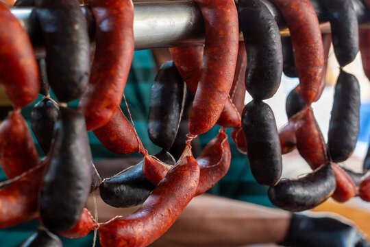 Close-up of spicy red chorizo and dark morcilla sausages hanging at a traditional market stall.