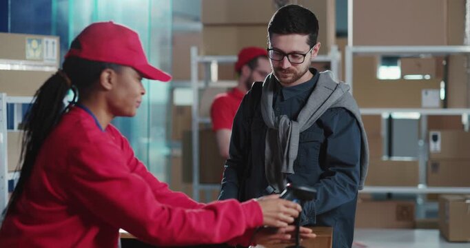 Multi-race couple of cooperative coworkers in red uniform servicing post parcel boxes to diverse clients in office workshop. Concept for post delivery services.