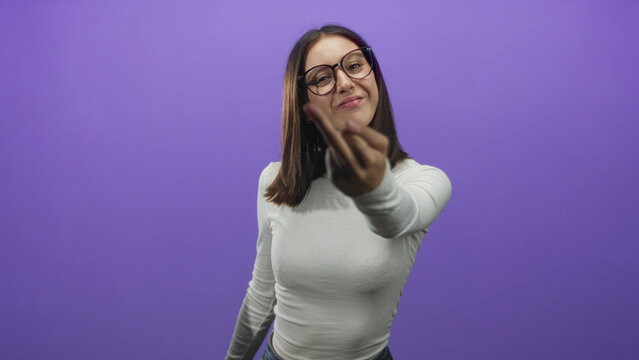 Woman flips middle finger to camera in studio wearing glasses and white long sleeve top with jeans against purple backdrop; defiance attitude.