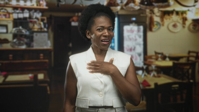 Woman in white vest placing hand on chest in a restaurant building with wooden tables and shelves; surprise gratitude.