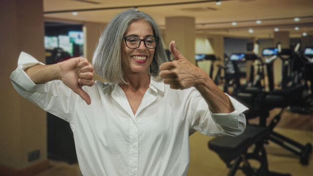 Woman showing hands with one thumb up and one thumb down inside a gym building; ambivalence decision.