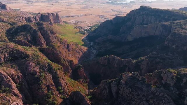 Drone footage reveals dramatic rocky canyon landscape of Sierra Madre Occidental mountain range in Durango, Mexico. Steep cliffs with sparse vegetation overlook vast agricultural plains below.