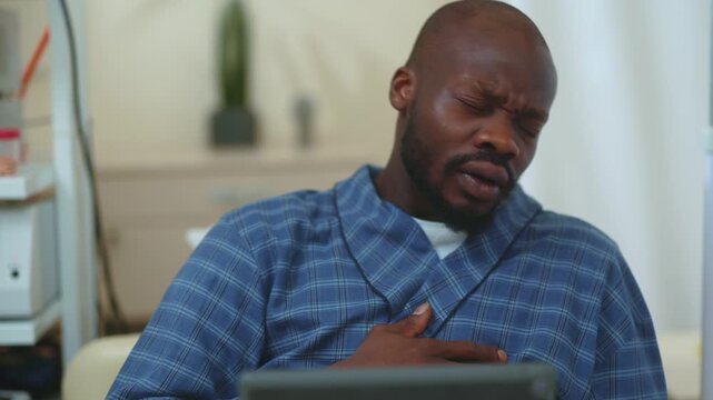 African young patient in hospital bed browsing digital tablet and suddenly suffering terrible chest pain. Disease symptoms. Unhealthy person. Healthcare and influenza.