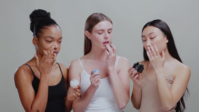 Diverse three skincare models applying eye cream. face moisturizer and lip balm trying new cosmetic products posing isolated on background. Healthy skin concept.