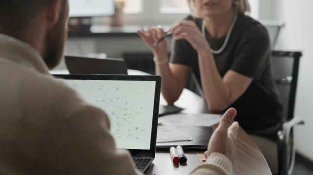 Tilt shot of unrecognizable man sitting at desk and looking at his colleague while they discussing business plans