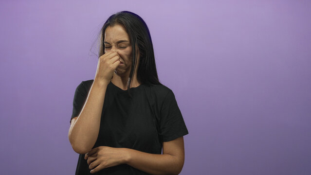 Woman pinches nose and grimaces in a purple studio with a visible nostril pinch; disgust odor issue.